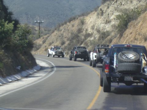 1985 Ford Ranger - A convoy of off-road trucks, including a 1985 Ford Ranger, navigates a scenic mountain road.