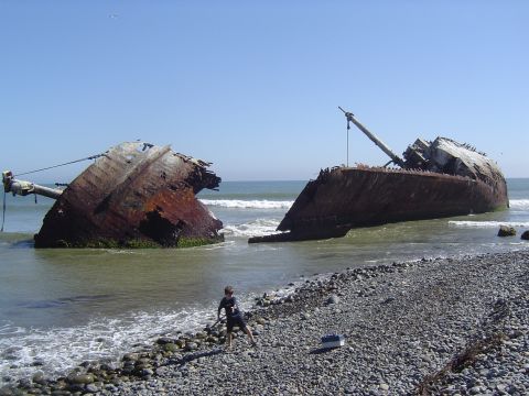 1985 Ford Ranger - A shipwreck lies broken on the shore under a clear blue sky.