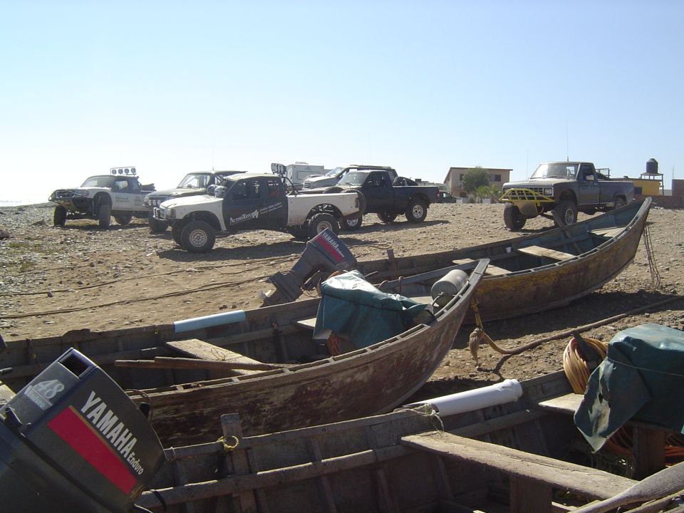 Several pickup trucks parked on a beach near fishing boats