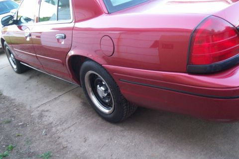 2001 Ford Crown Victoria - A red 2001 Ford Crown Victoria sedan is viewed from the rear driver's side, showing its body style and wheels.
