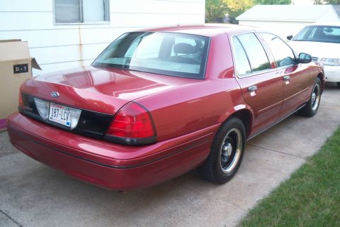 2001 Ford Crown Victoria - Rear view of a red 2001 Ford Crown Victoria sedan parked next to a white vehicle.