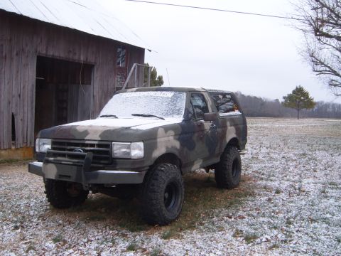 1988 Ford Bronco - A camouflaged Ford Bronco sits in a snowy field with a barn in the background.