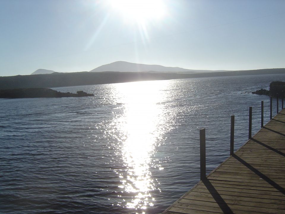 Water reflecting sun, wooden dock, distant hills