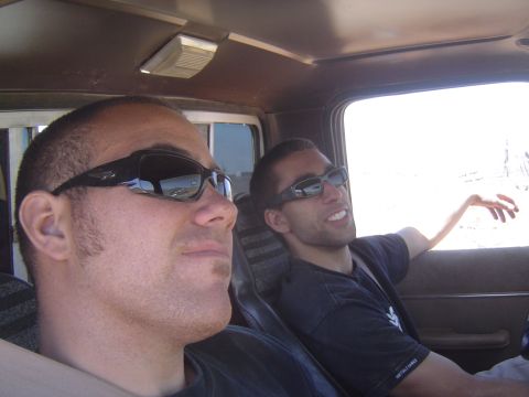 1985 Ford Ranger - Two men wearing sunglasses ride inside a truck cab, with the bright sun visible through the window.