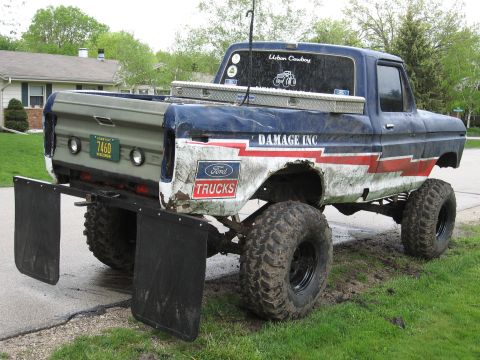 1977 Ford F-150 - This lifted 1977 Ford F-150 features large off-road tires, prominent mud flaps, and custom "Damage Inc." graphics.