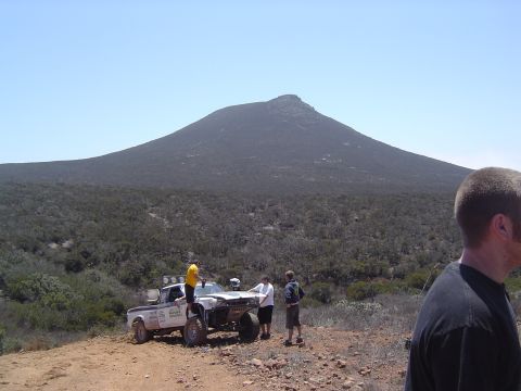 1985 Ford Ranger - A modified pickup truck sits on a dusty trail, with a mountain looming behind it and several people observing.