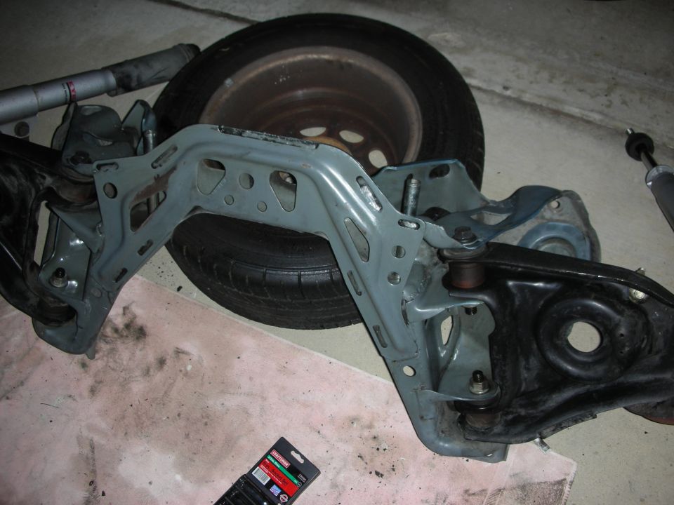 Removed suspension crossmember with control arms leaning on a tire in a garage
