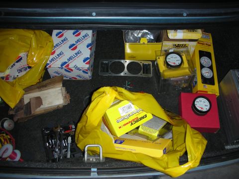 1990 Ford Mustang - The trunk of a vehicle contains various automotive parts, including engine components, suspension parts, and multiple gauges.
