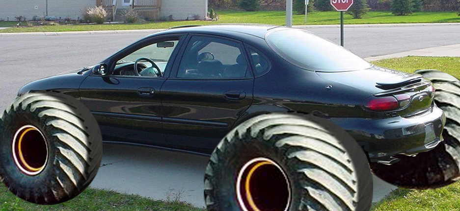 Black Ford Taurus sedan mounted on huge monster-truck tires by a stop sign