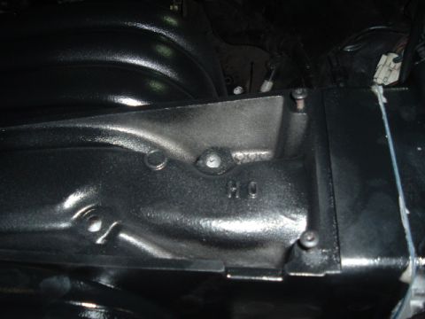 1989 Ford LTD Crown Victoria - Close-up engine bay shot of a black plastic intake manifold and adjacent cover, with cast ribbing and raised lettering visible under low li…