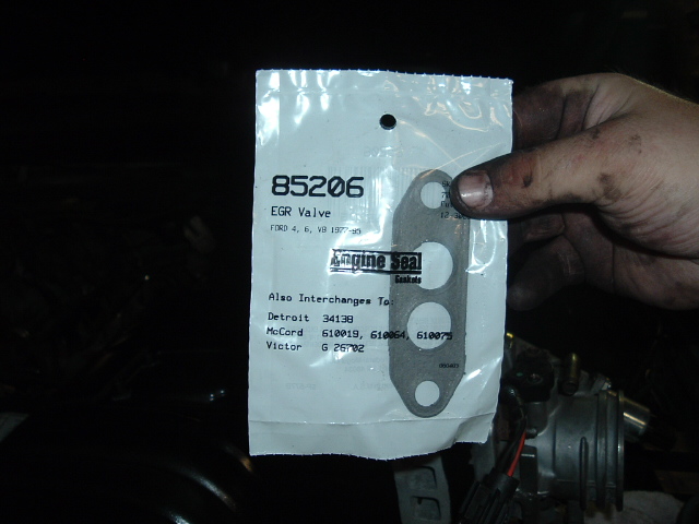 Engine Seal 85206 EGR valve gasket in sealed package for Ford engines, held over an engine bay