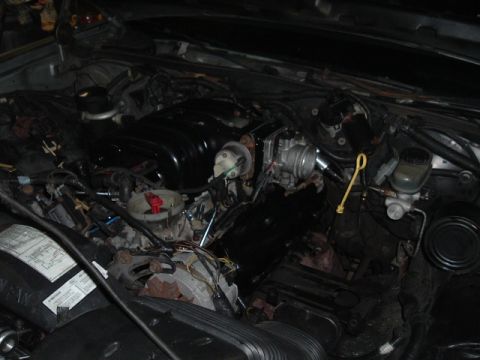 1989 Ford LTD Crown Victoria - Engine bay mid-project in a garage: a V8 wearing a black intake plenum and bare throttle body sits with wiring harnesses unplugged and drap…