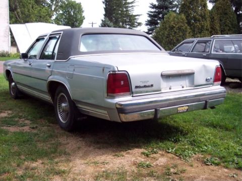1990 Ford Crown Victoria LTD - The rear of a 1990 Ford Crown Victoria LTD is shown, with a second vehicle partially visible in the background.