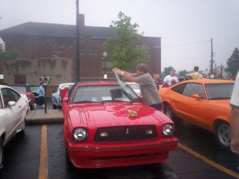 1978 Ford Mustang II - A red 1978 Ford Mustang II is being cleaned while an orange Mustang II is parked nearby.