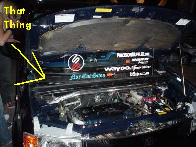 1993 Ford Taurus - The engine compartment of a Scion xB is visible, with various stickers adorning the hood lining.