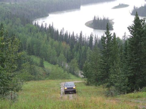 1988 Ford Bronco - A 1988 Ford Bronco navigates a dirt track through a wooded area beside a wide river.