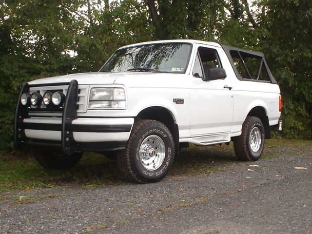 White Ford Bronco with a brush guard and four auxiliary lights parked on a gravel surface