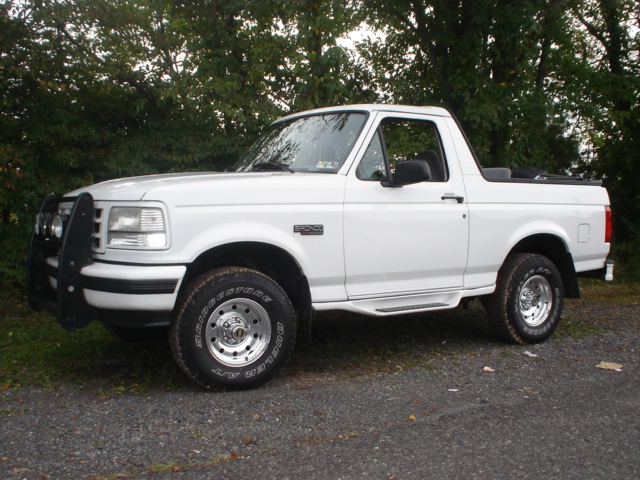 White 1995 Ford Bronco with a black bull bar and running boards, parked on gravel