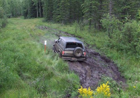 1988 Ford Bronco - A dark-colored SUV navigates a challenging muddy trail, its spare tire mounted on the rear door.