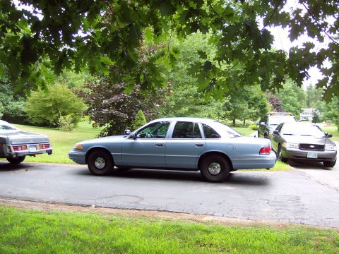 2001 Ford Crown Victoria - A light blue 2001 Ford Crown Victoria is parked on a driveway with other vehicles nearby.
