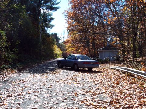 2001 Ford Crown Victoria - A blue 2001 Ford Crown Victoria is parked on a road strewn with autumn leaves, with trees and a small building in the background.