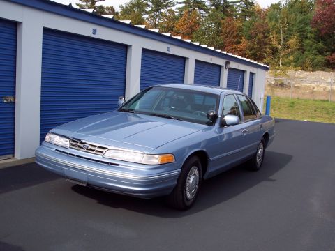 2001 Ford Crown Victoria - A blue 2001 Ford Crown Victoria is parked outside a row of blue storage unit doors.