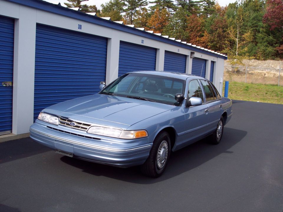 Blue 2001 Ford Crown Victoria parked in front of storage units