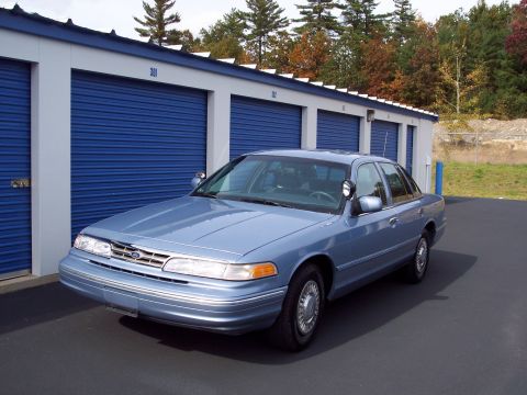 2001 Ford Crown Victoria - 2001 Ford Crown Victoria police car parked outside storage units on a cloudy day.