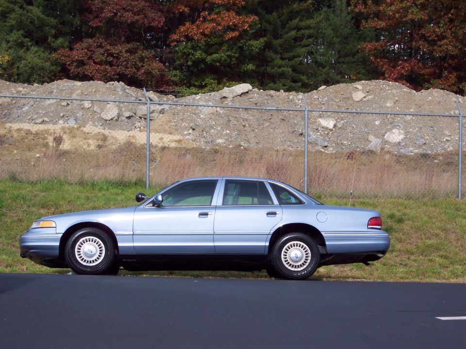 Side view of a light blue 2001 Ford Crown Victoria sedan parked on a grassy verge