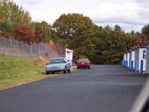 2001 Ford Crown Victoria - Two cars are parked on an asphalt lot next to storage units.