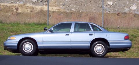 2001 Ford Crown Victoria - A light blue 2001 Ford Crown Victoria sedan is shown from the side, parked near a grassy embankment.