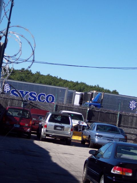 2001 Ford Crown Victoria - Several vehicles are parked in front of a Sysco building under a clear blue sky.