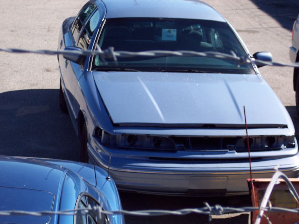 Light blue 2001 Ford Crown Victoria with hood open, missing grille and headlights, viewed from front