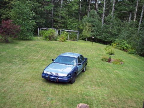 2001 Ford Crown Victoria - A two-tone sedan sits on a sloped lawn with trees in the background.