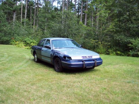 2001 Ford Crown Victoria - A 2001 Ford Crown Victoria with mismatched body panels sits in a grassy field.