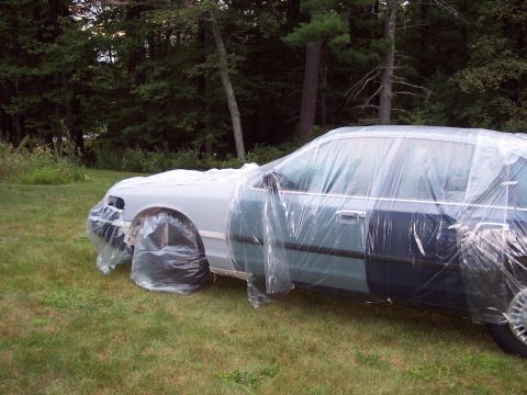 2001 Ford Crown Victoria - A 2001 Ford Crown Victoria is covered in plastic sheeting, likely for protection during a paint job or storage.