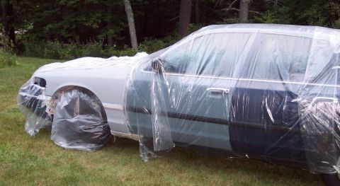2001 Ford Crown Victoria - A car is covered in plastic sheeting, likely for painting or protection, outdoors on a grassy area.