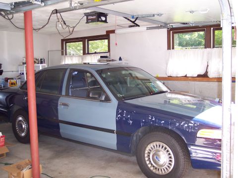 2001 Ford Crown Victoria - A two-tone blue 2001 Ford Crown Victoria is parked inside a garage, showing its front passenger side.