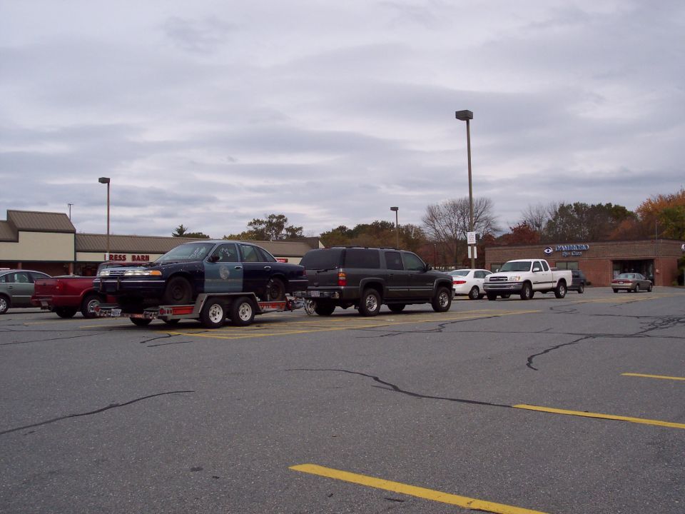 Charcoal Chevrolet Suburban towing a trailer with a dark Ford Crown Victoria in a parking lot.