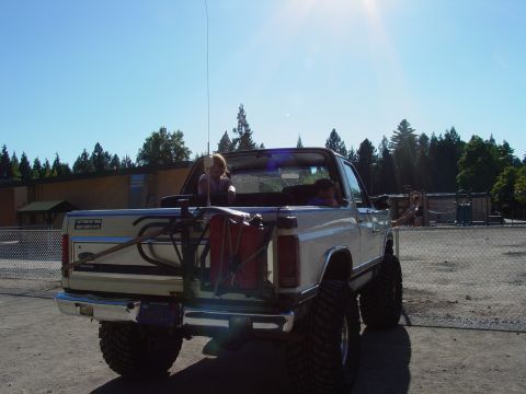 1986 Ford Bronco - A white pickup truck with people in the bed is parked outdoors on a sunny day.