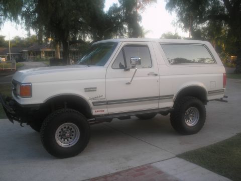 1990 Ford Bronco - Side view of a white 1990 Ford Bronco, lifted with off-road tires and a custom front bumper.