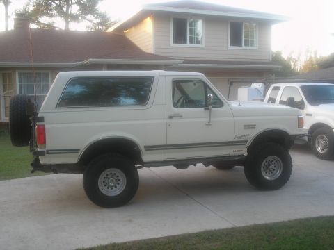 1990 Ford Bronco - A white 1990 Ford Bronco is parked in a driveway with a house in the background and another truck behind it.