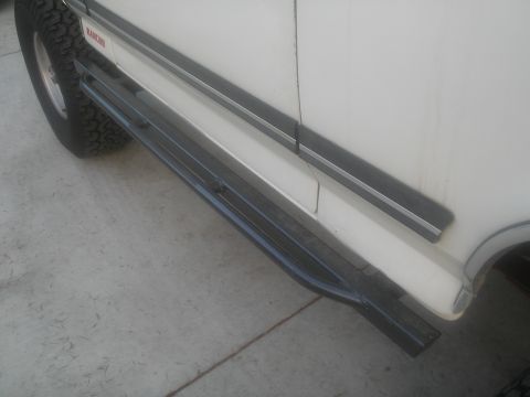 1990 Ford Bronco - Side view of a white SUV showing its running boards and a portion of the tire.