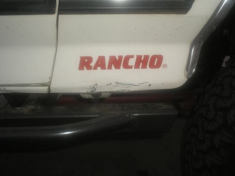 1990 Ford Bronco - Close-up of a white SUV's side panel displaying a red "RANCHO" decal and visible scuff marks.