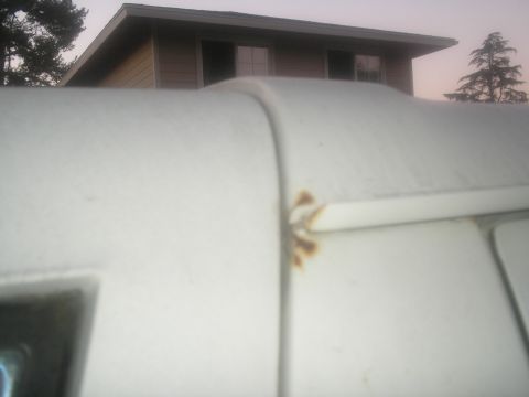1990 Ford Bronco - The photo shows the top of a white vehicle with visible rust on the trim, against a backdrop of a house and trees.