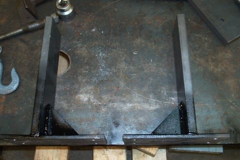 1983 Ford Bronco - Two custom metal brackets are shown on a workbench, ready for installation or further modification.
