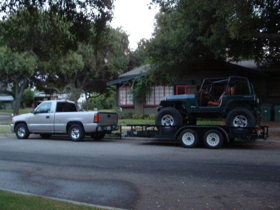 Dark green Jeep Wrangler on a trailer, towed by a silver pickup truck