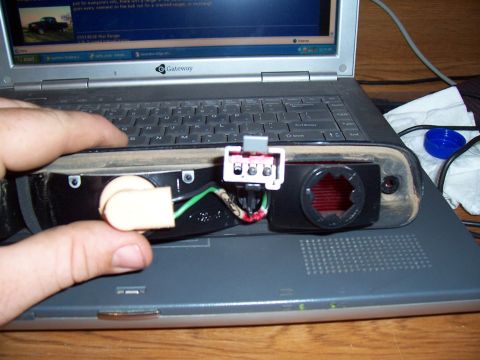 2003 Ford Ranger - A person is holding a vehicle's tail light assembly, showing its internal wiring and bulb socket, over a laptop.