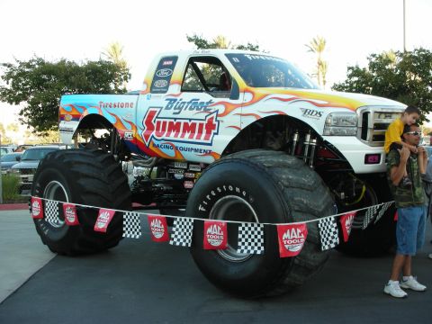 1998 Ford Crown Victoria - A large monster truck with custom paint and oversized tires is parked outdoors, with spectators nearby.
