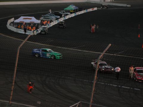 1998 Ford Crown Victoria - Multiple race cars are on a track during an event, with tents and people visible.